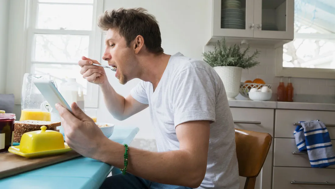 غذا خوردن مرد پشت میز در حال خواندن